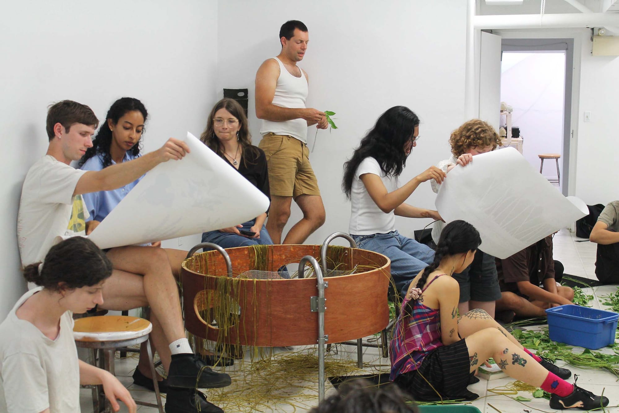A group of people in a white-walled room with a circular metal-and-wooden object in the centre. Some are looking at large sheets of paper.