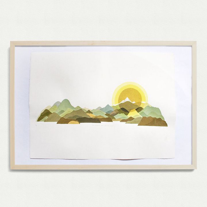 Photo of a framed art print showing the sun rising behind a mountain range
