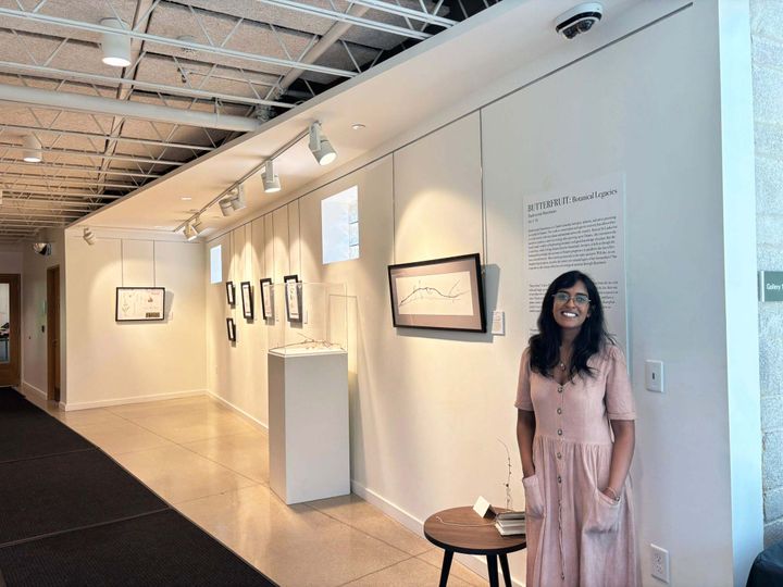 A person standing next to a wall of hanging art in a gallery