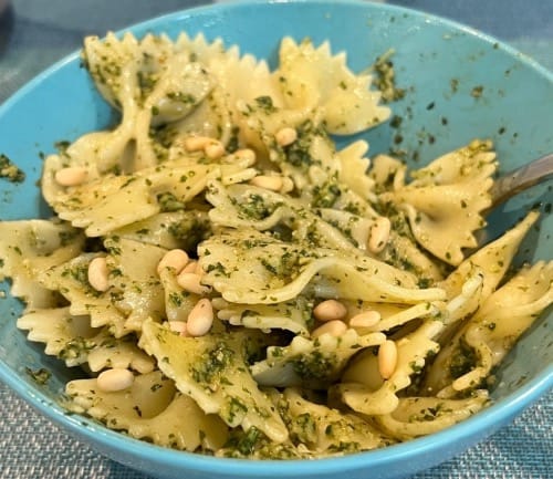 blue bowl filled with bowtie pasta in pesto sauce with pine nut garnish