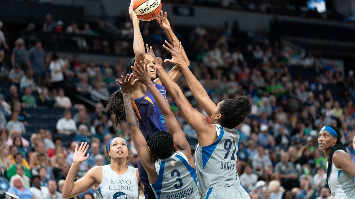 WNBA-spiller skyter over forsvarere i kamp.