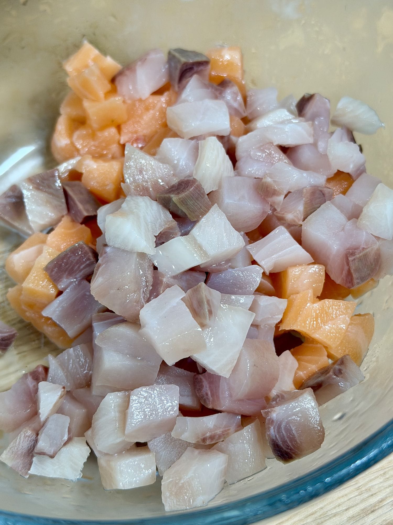 Finely diced yellowtail and salmon in a glass bowl showing clean cube faces.