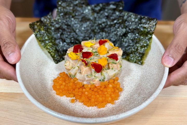 Hands presenting a bowl of yellowtail and salmon tartare with salmon roe and toasted nori.
