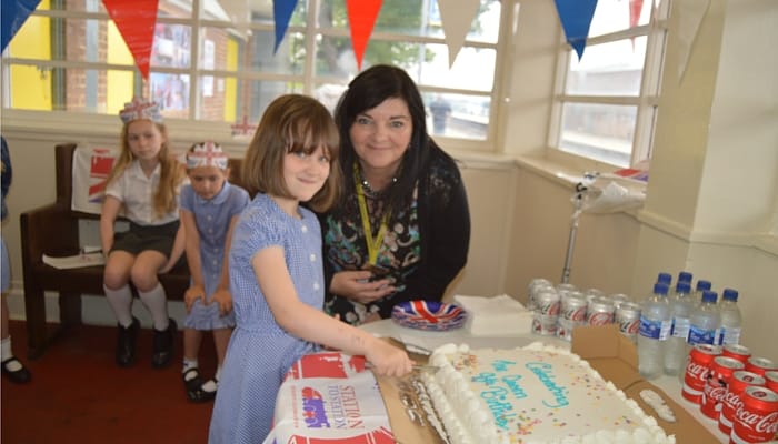 Sally Ralston, from Merseyrail, cutting the Queen's birthday cake with local schoolchildren