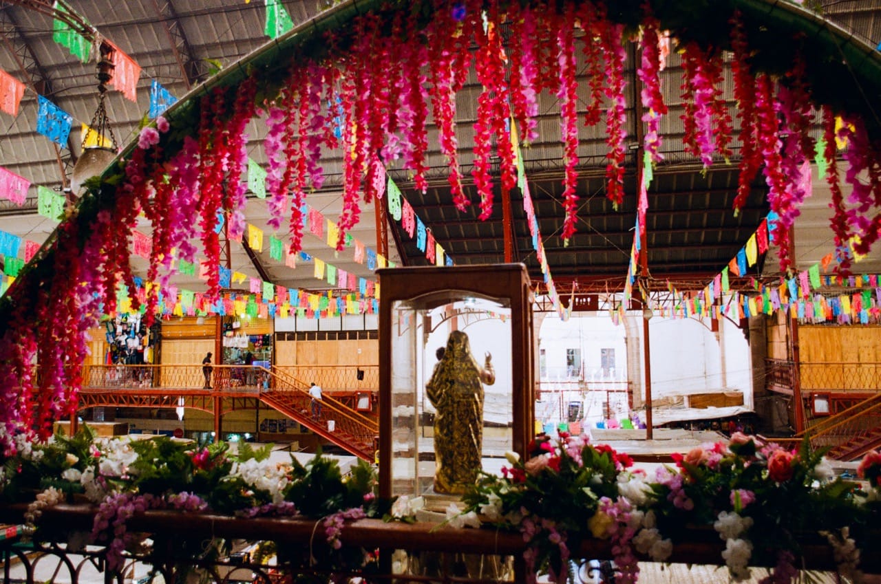 a color photo of some sort of important-to-Catholics figurine in a glass box under pink floral arch decor, overlooking the Mercado Hidalgo