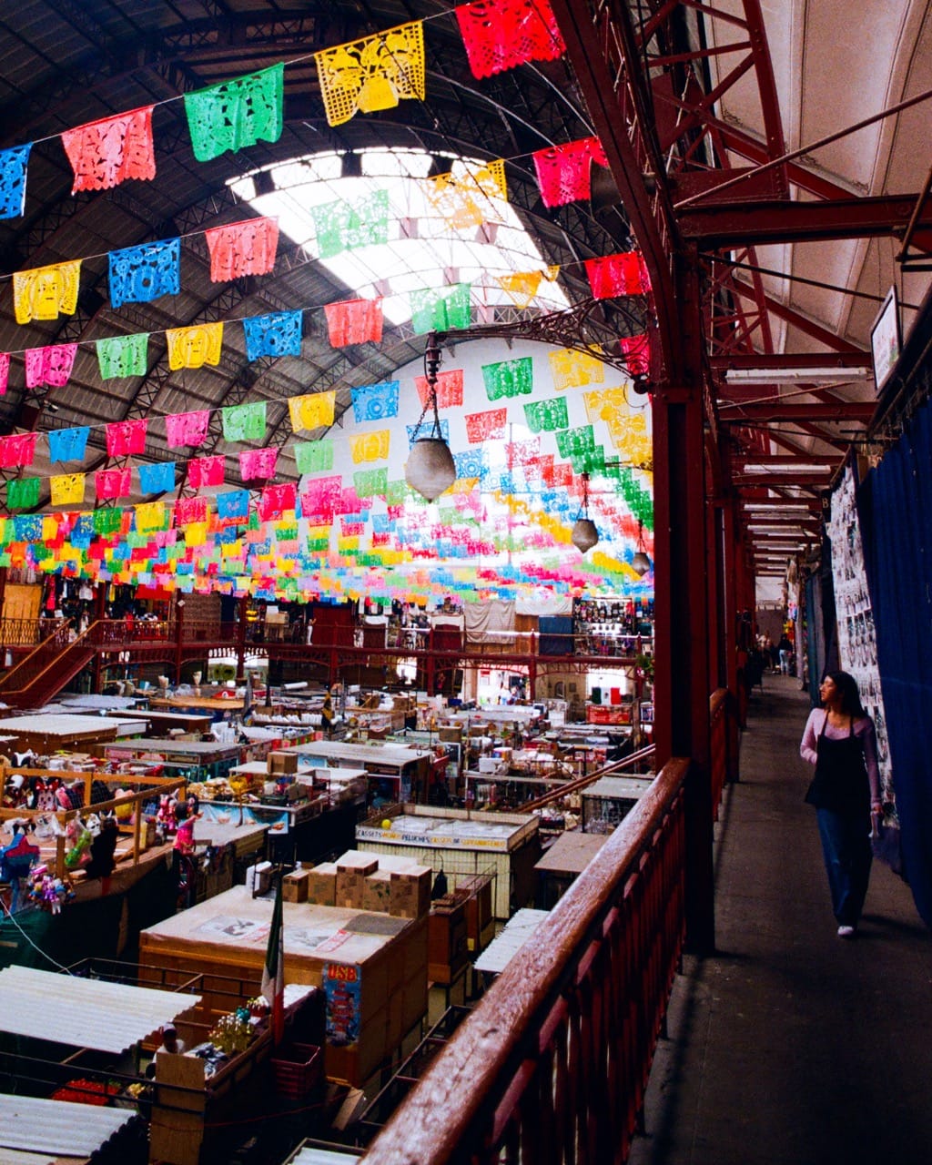 a photo of the interior of Mercado Hidalgo, with a woman walking along the second-floor landing overlooking the main market hall across the rail