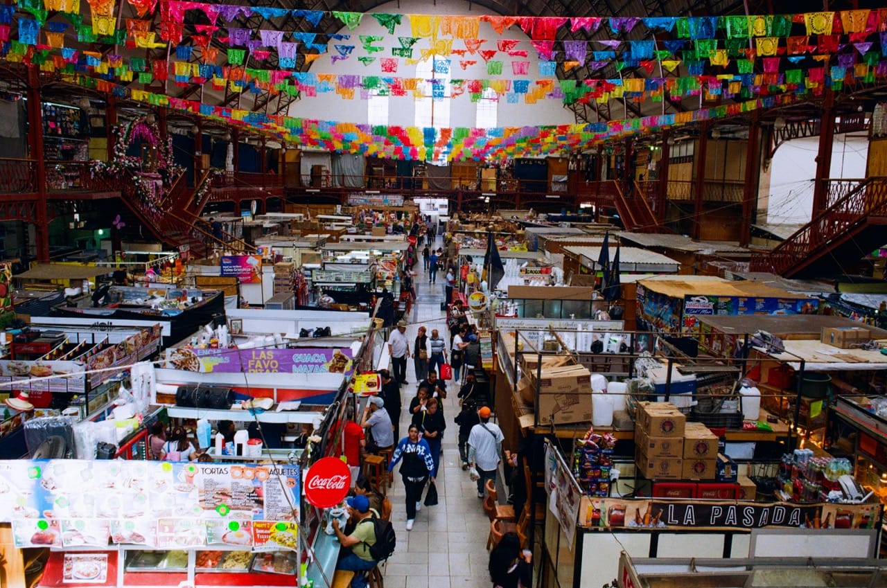 The interior of the Mercado Hidalgo, with rows of vendors on the floor underneath rows of colorful flags strung overhead
