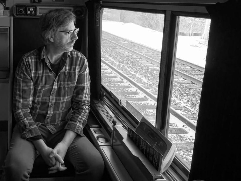 a black and white photograph of J. Mark in an Amtrak Roomette, looking pensively out the window at passing train tracks dusted with snow