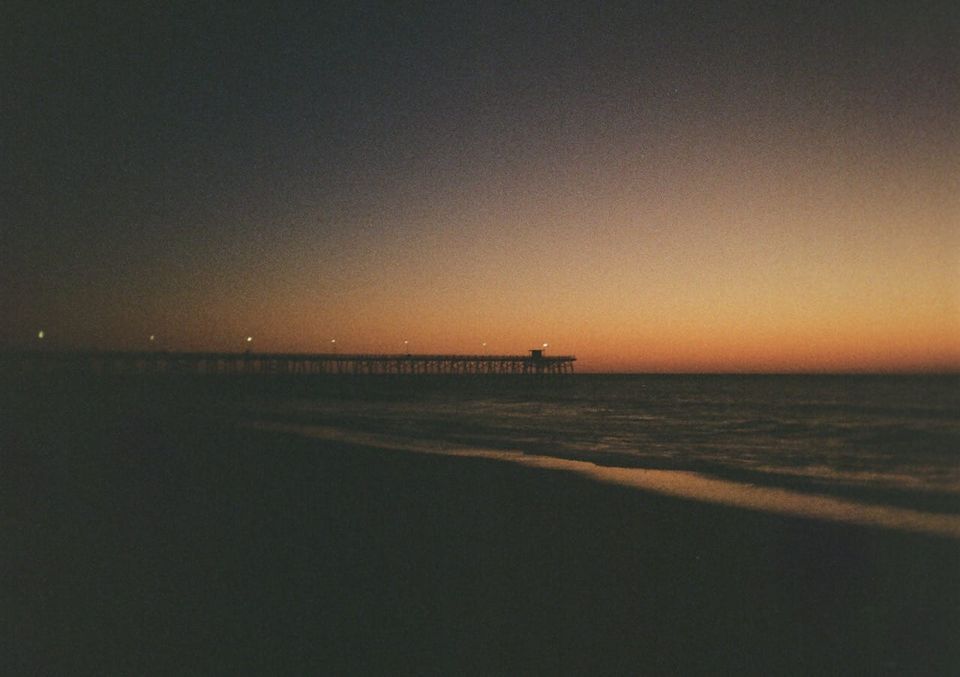 a grainy color photo of the sun about to rise over the Atlantic Ocean, with Kure Beach Pier in the distance