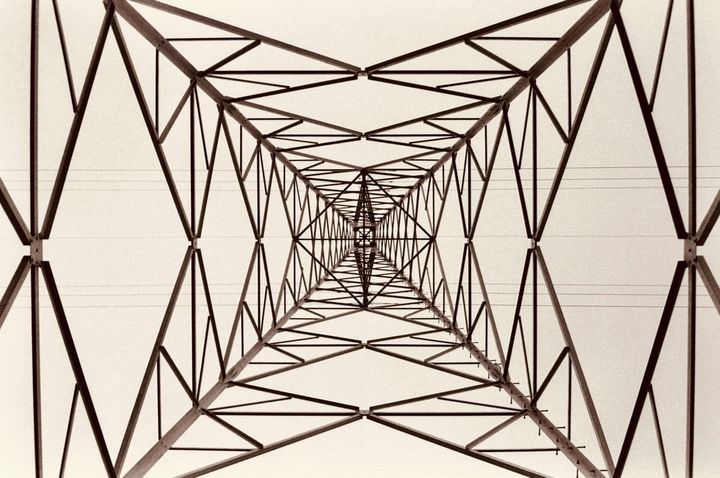Looking up through the steel lattice of an electricity transmission tower, representing the interconnected roles and responsibilities in an enterprise AI governance structure.