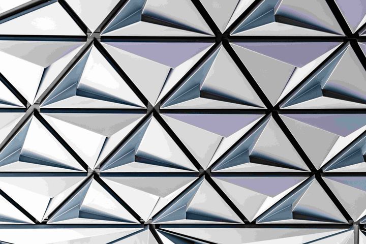 Geometric metallic facade with repeating triangular panels and dark structural framing, representing the layered and interconnected cost structures beneath enterprise AI pricing.