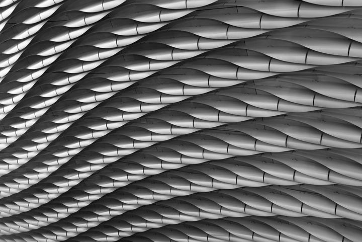 Interlocking metallic wave panels on a building facade, representing the layered and compounding cost structures of enterprise AI vendor exit
