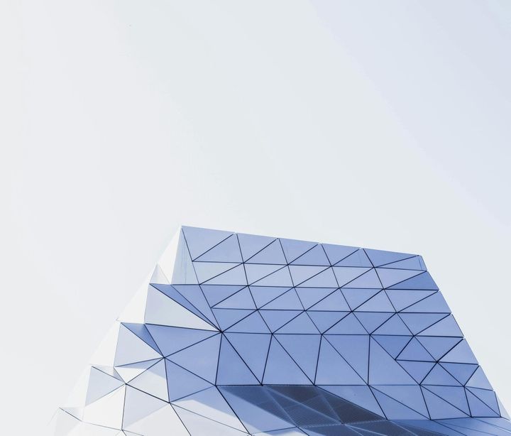Geometric glass facade with triangular panels against a pale sky, representing the structured unit economics of enterprise AI cost per query