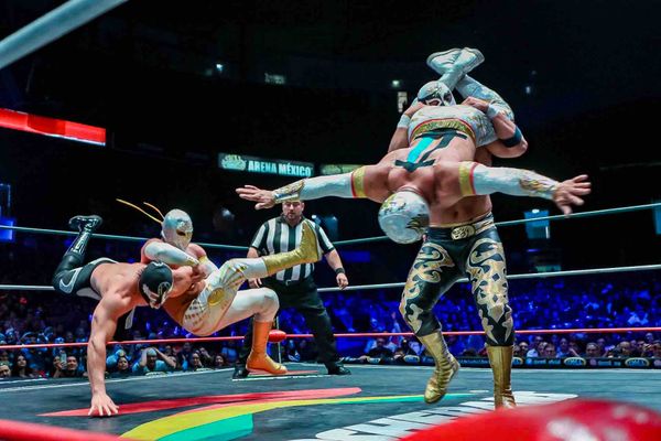Lucha Libre wrestling featuring two pairs of wrestlers and a referee in a ring in front of a large crowd