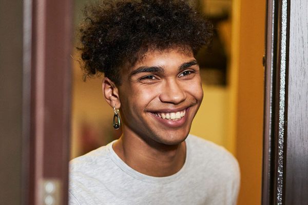 A young person smiling as they welcome someone at the door.