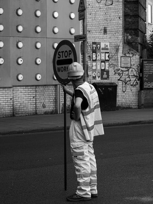 Construction worker holding a sign that says Stop Workers wearing a vest