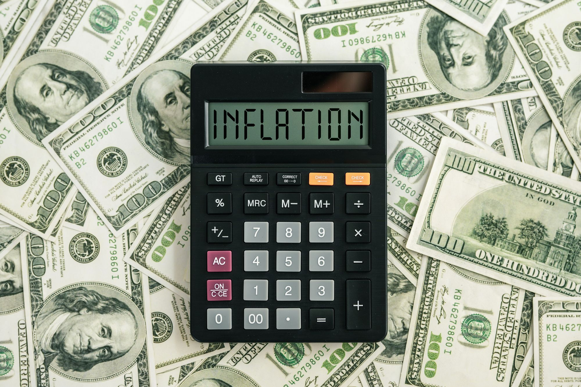 Calculadora mostrando "INFLATION" sobre billetes de 100 dólares, simbolizando el aumento de costos