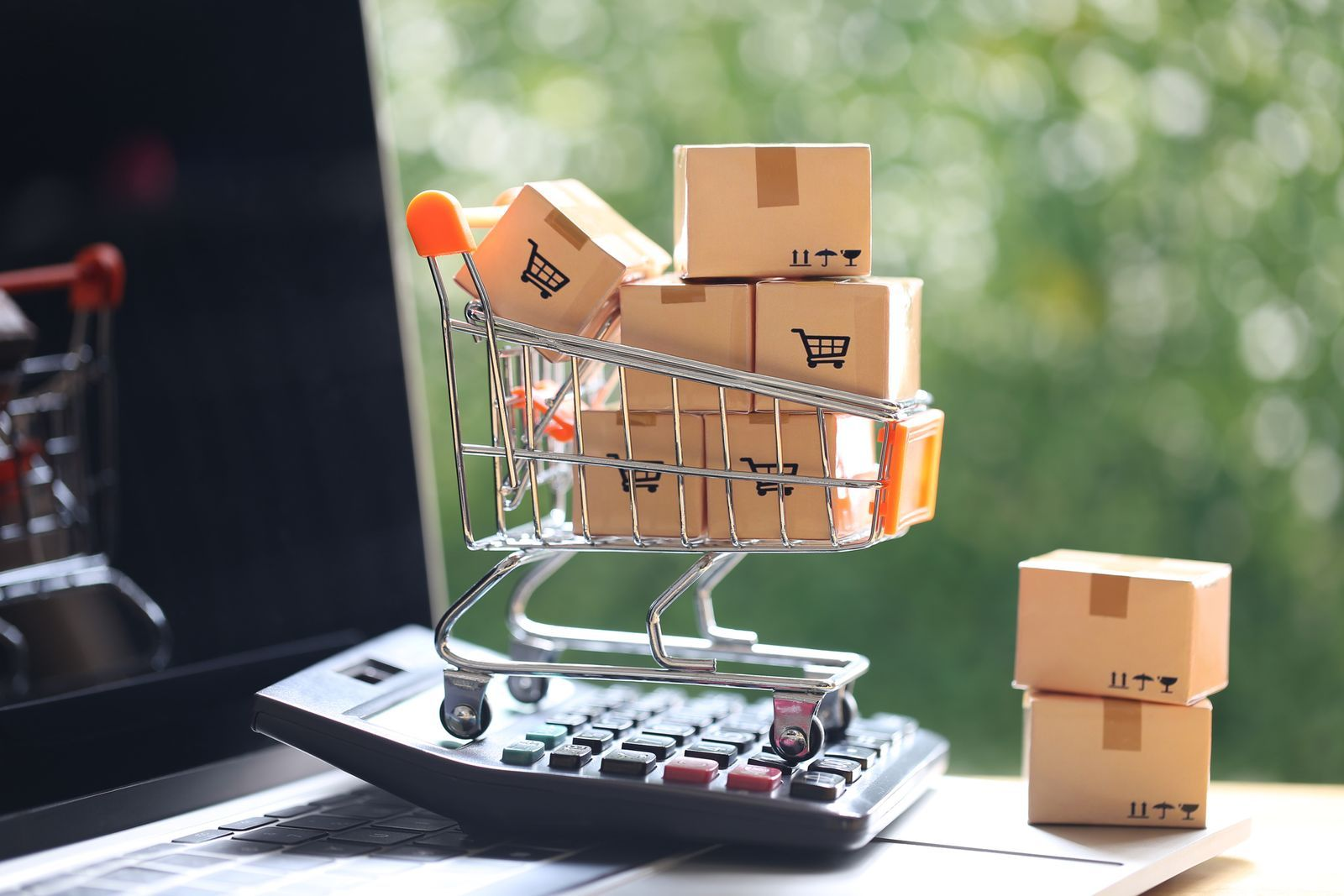Carrito en miniatura y cajas de envío sobre un portátil y una calculadora