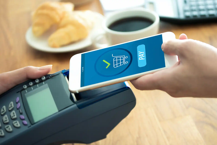 Cliente realizando un pago móvil con su smartphone al acercarlo a un lector RFID en el punto de venta