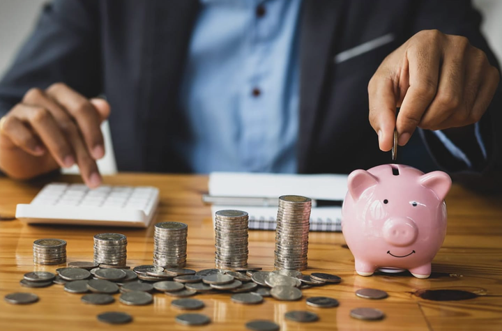 Empresario contando monedas y billetes mientras toma notas sobre las ganancias del negocio