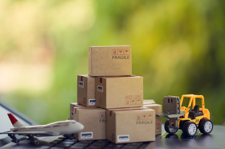 Carretilla elevadora moviendo una caja de cartón sobre un teclado de portátil con fondo verde natural