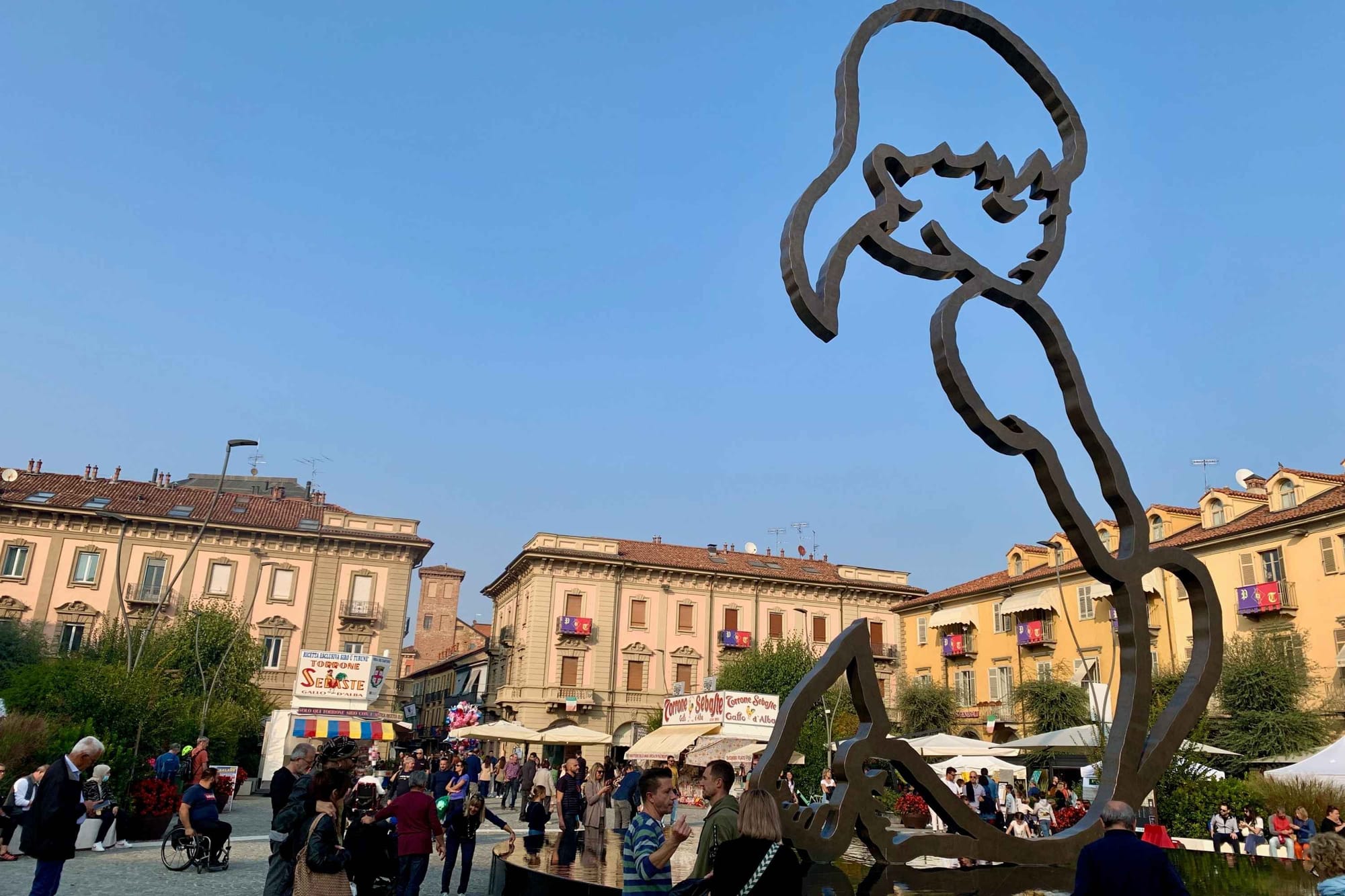 The main square and "Alba" statue in Alba with market stalls in the background.