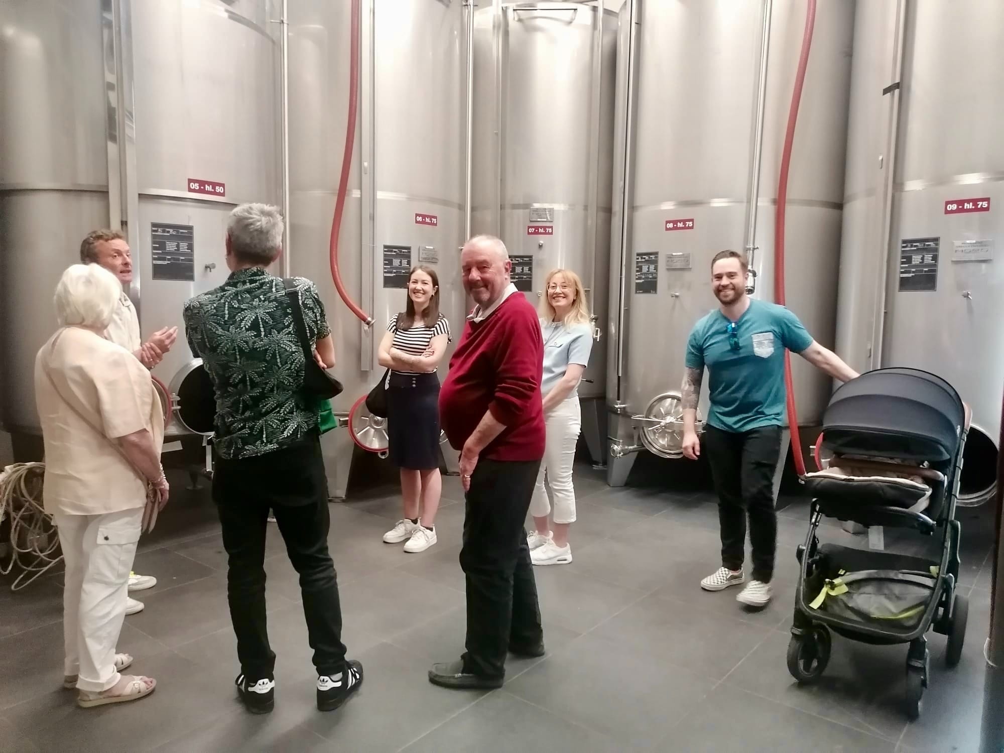 A group of people in a wine cellar, surrounded by stainless steel tanks