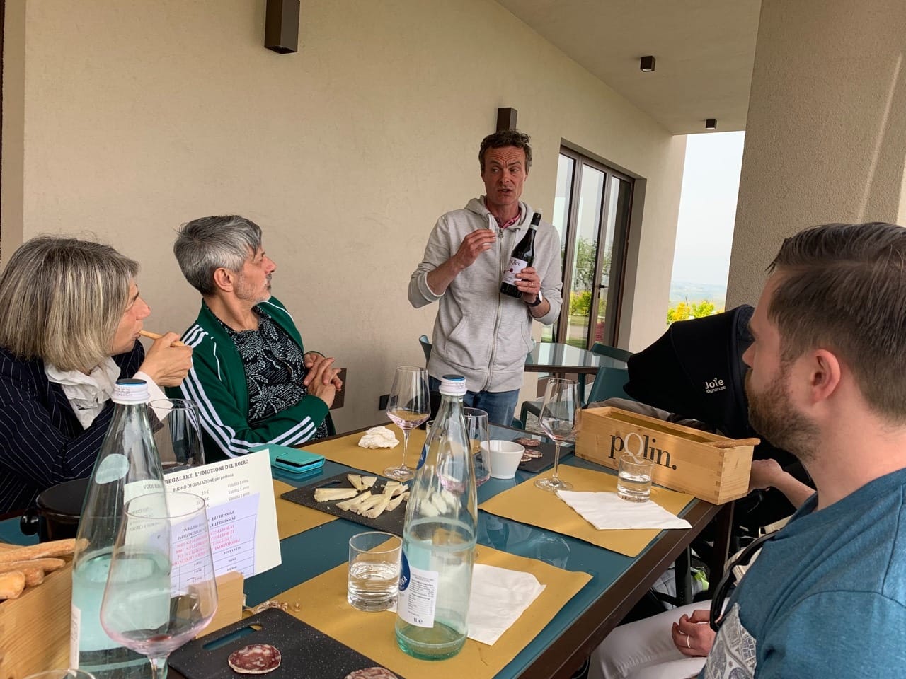 A man speaks with a bottle of wine in his hand while a seated group listens