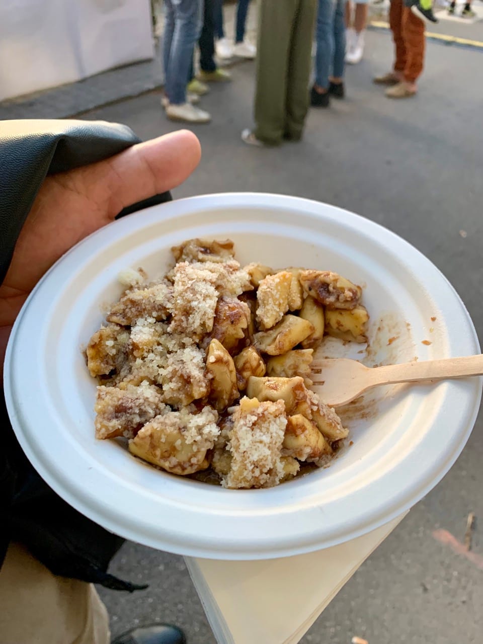 A hand holds up a white plate containing filled pasta topped with grated Parmesan cheese and a wooden fork.