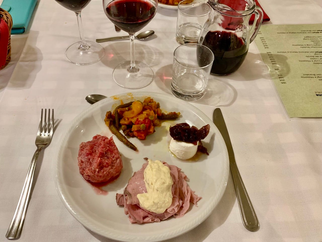 A plate with four Piedmontese antipasti, a jug of red wine, and two wine glasses