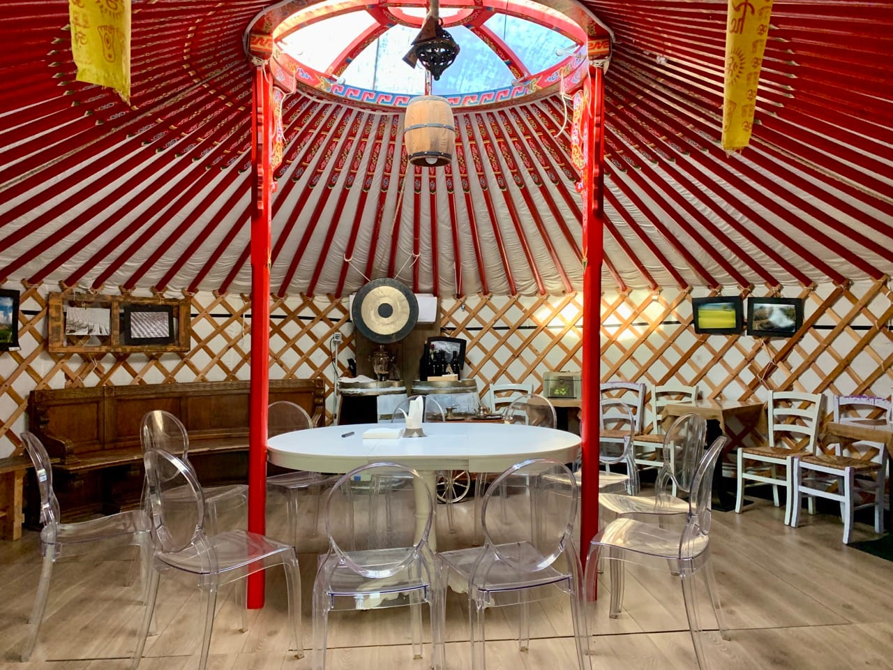 A circular room with a table and chairs in the middle. Photos of landscapes and a gong hang on the wall.