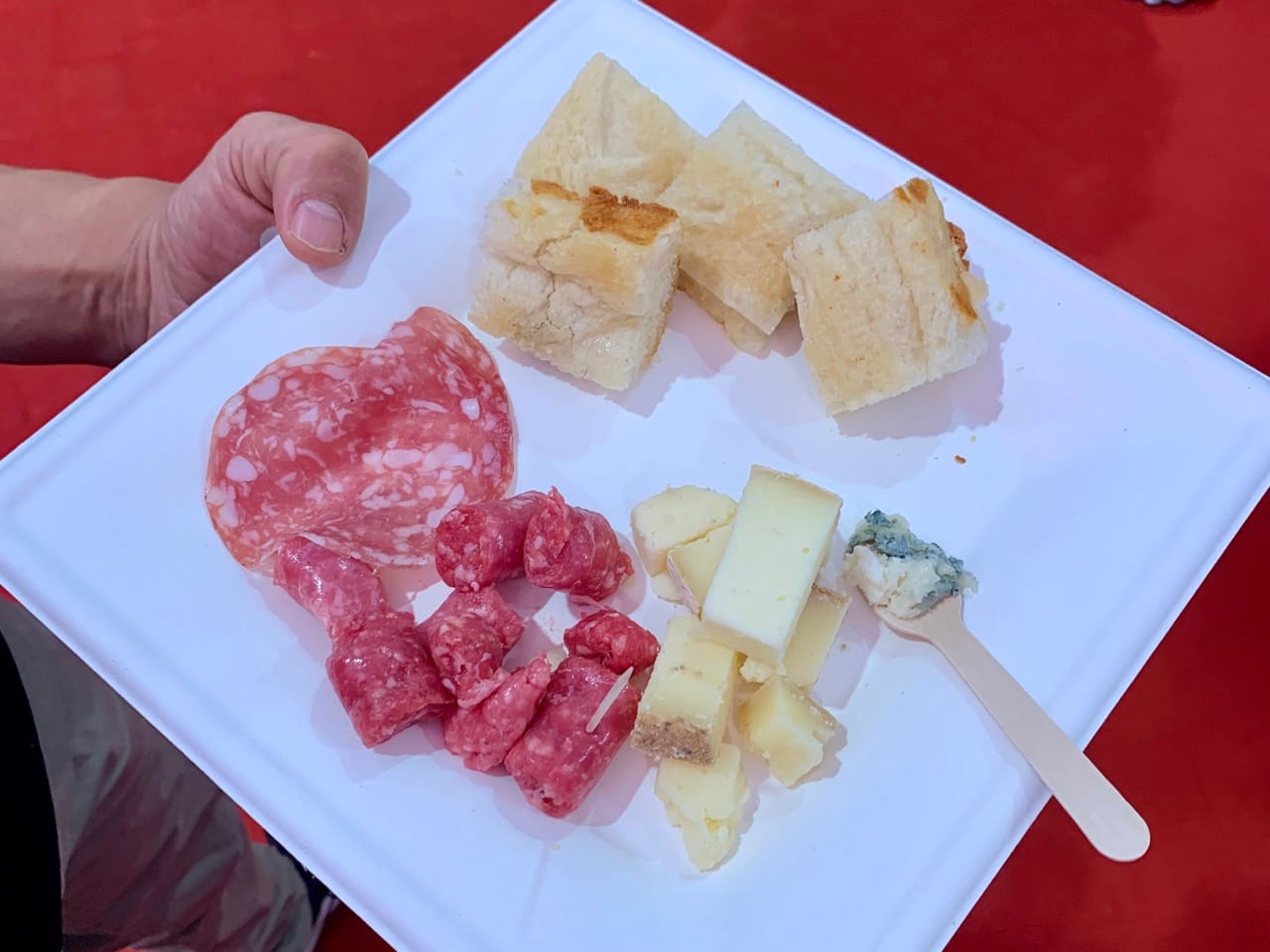 A square white plate with Bra sausage, 3 types of cheese, salame, and focaccia.