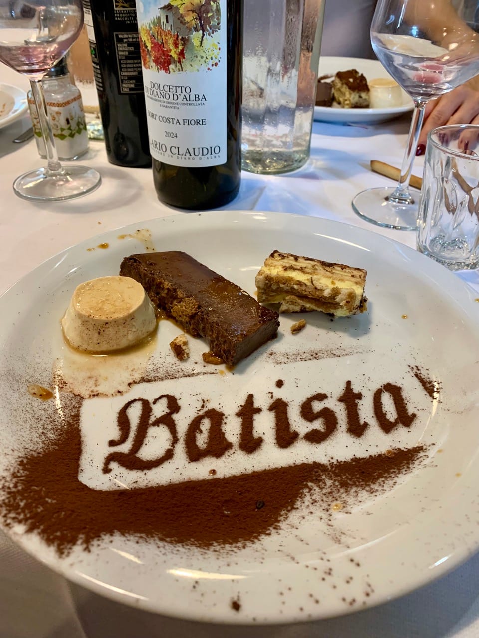 Panna cotta, bonet, and tiramisu on a plate with "Batista" written in cocoa powder.