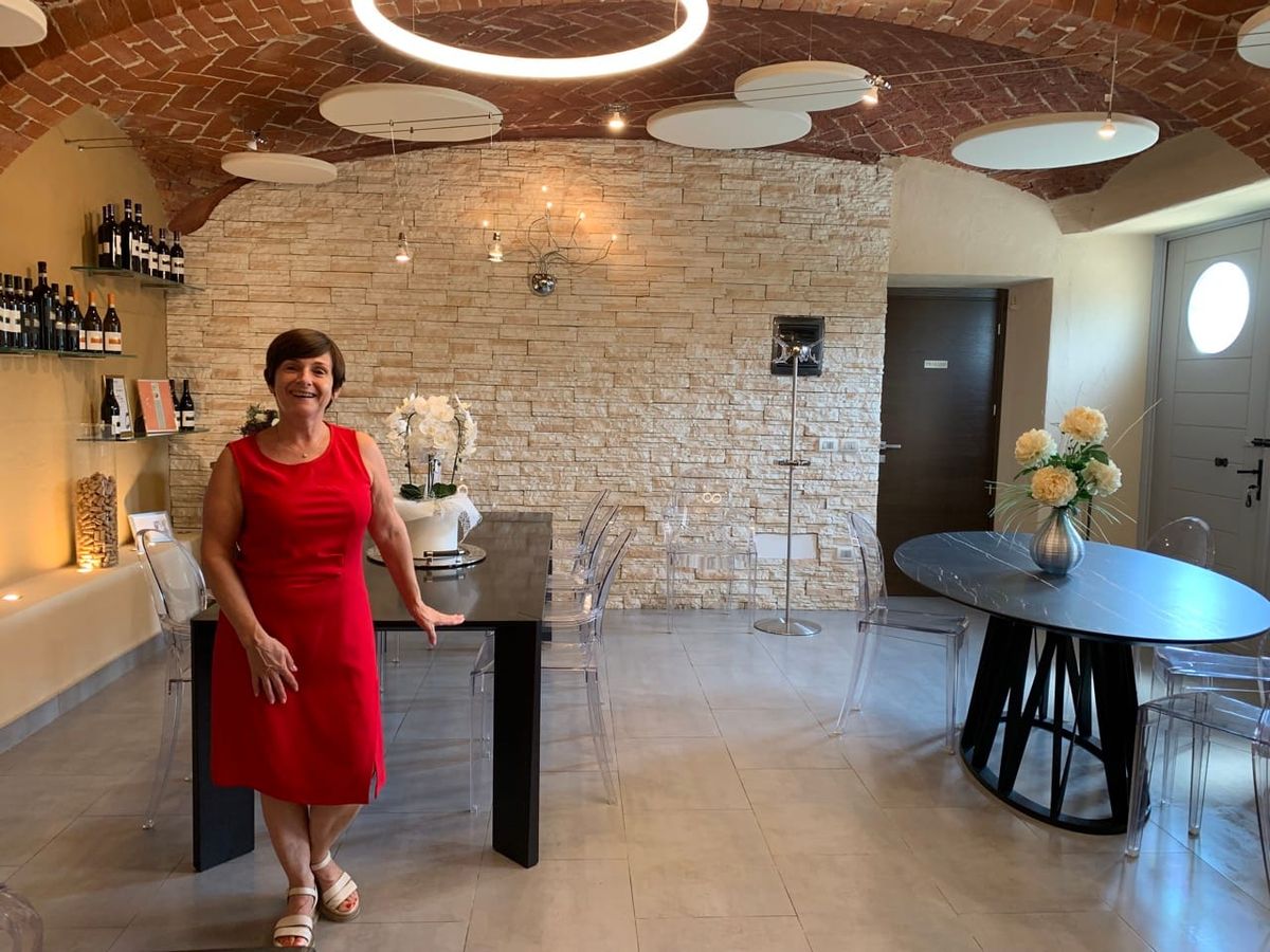 A woman in a red dress smiles while leaning on a table. Behind her are bottles of wine on the wall.
