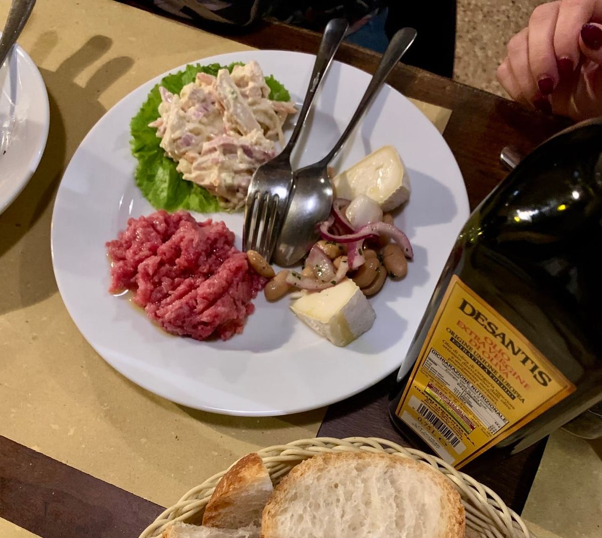 A plate with a selection of Piedmontese antipasti next to a basket of bread and a bottle of olive oil.