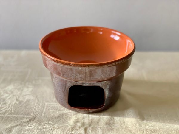 A small terracotta pot burner on a cream tablecloth with a white background.