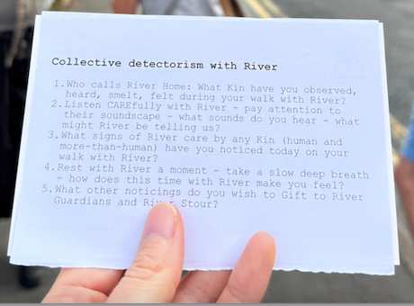 A white postcard held in a hand with 5 questions called Collective detectorism with River These prompts are for learning with River testing out a grammar of animacy