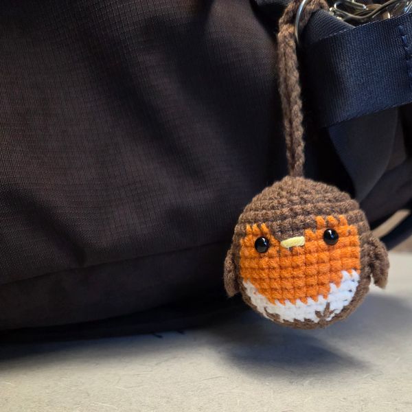 A crocheted European Robin hanging on the side of a backpack.