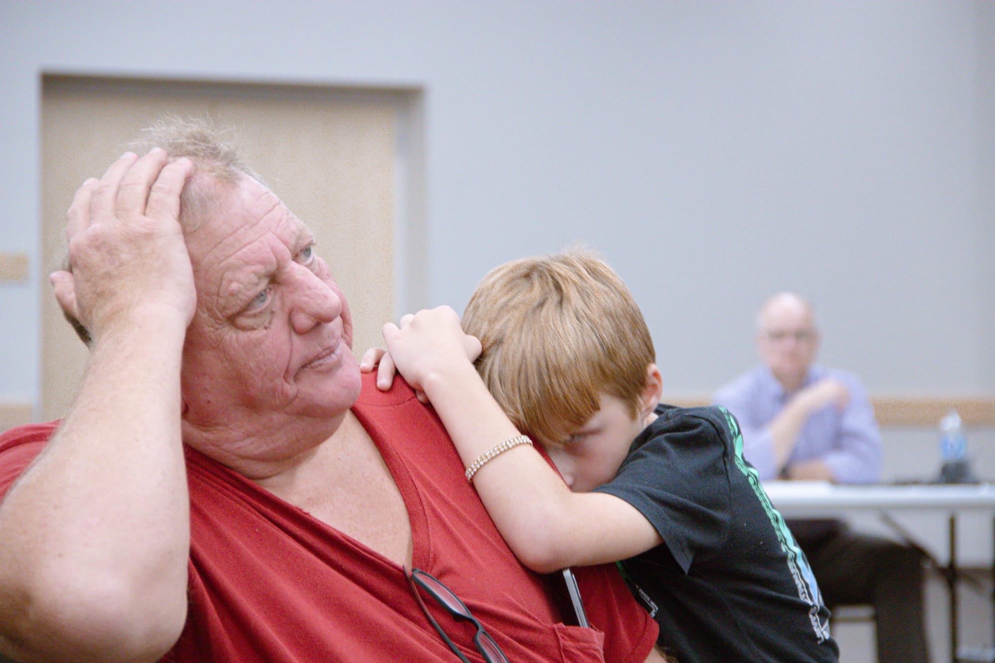A child in a black shirt lies on the shoulder of an older man in a red shirt