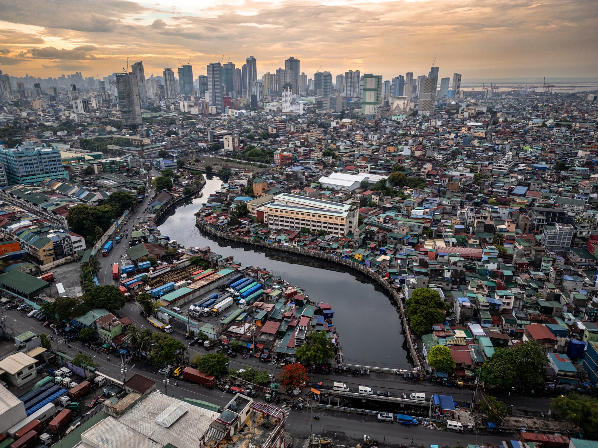 Aerial view of a densely populated urban area on both sides of a creek. In the distance is a large skyline and the ocean.