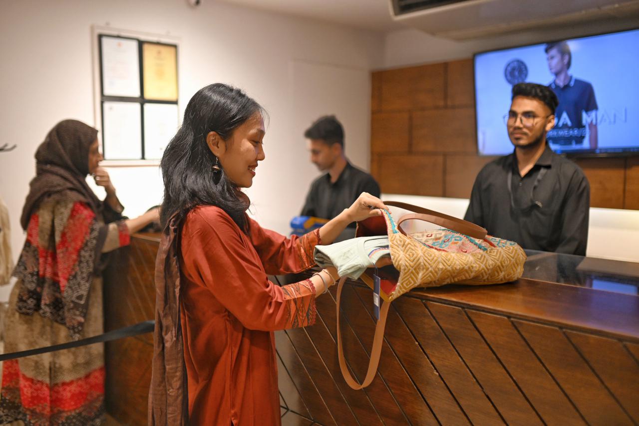 A smiling customer places her newly bought clothes inside her own reusable bag, while two shop employees stand in the background.