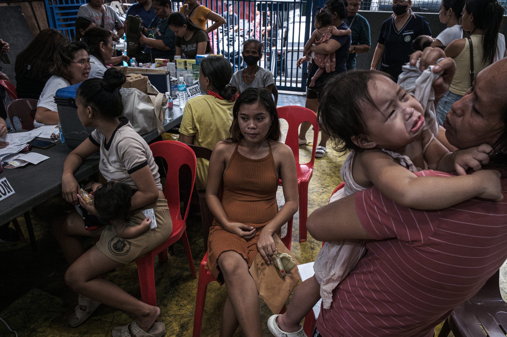 A woman sits in a chair, while other mothers hold their crying children.