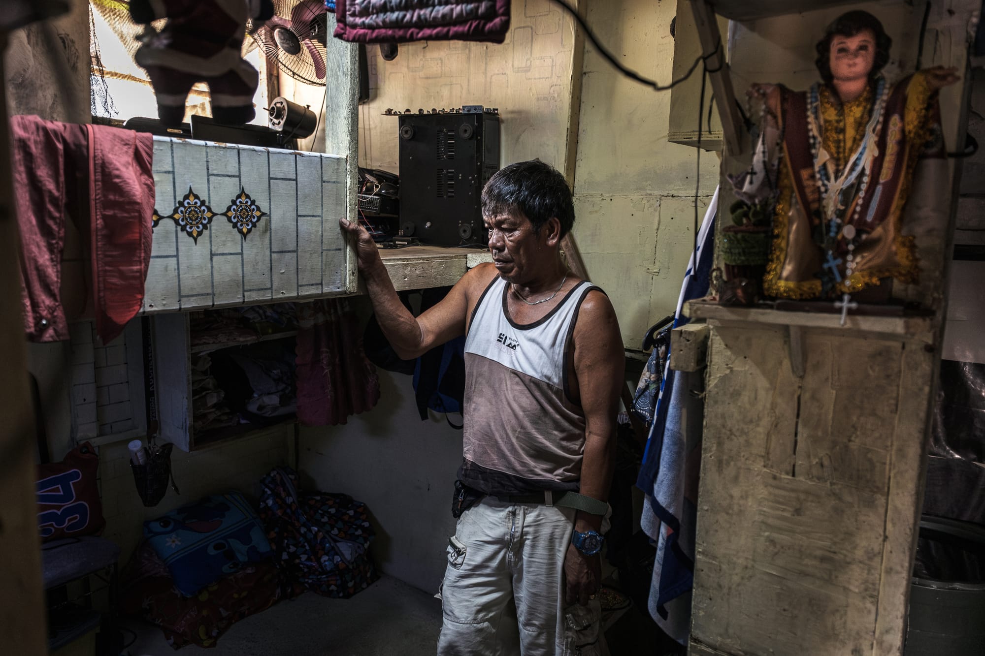 A Filipino man with short hair, a watch, and wearing a vest stands inside a small room.