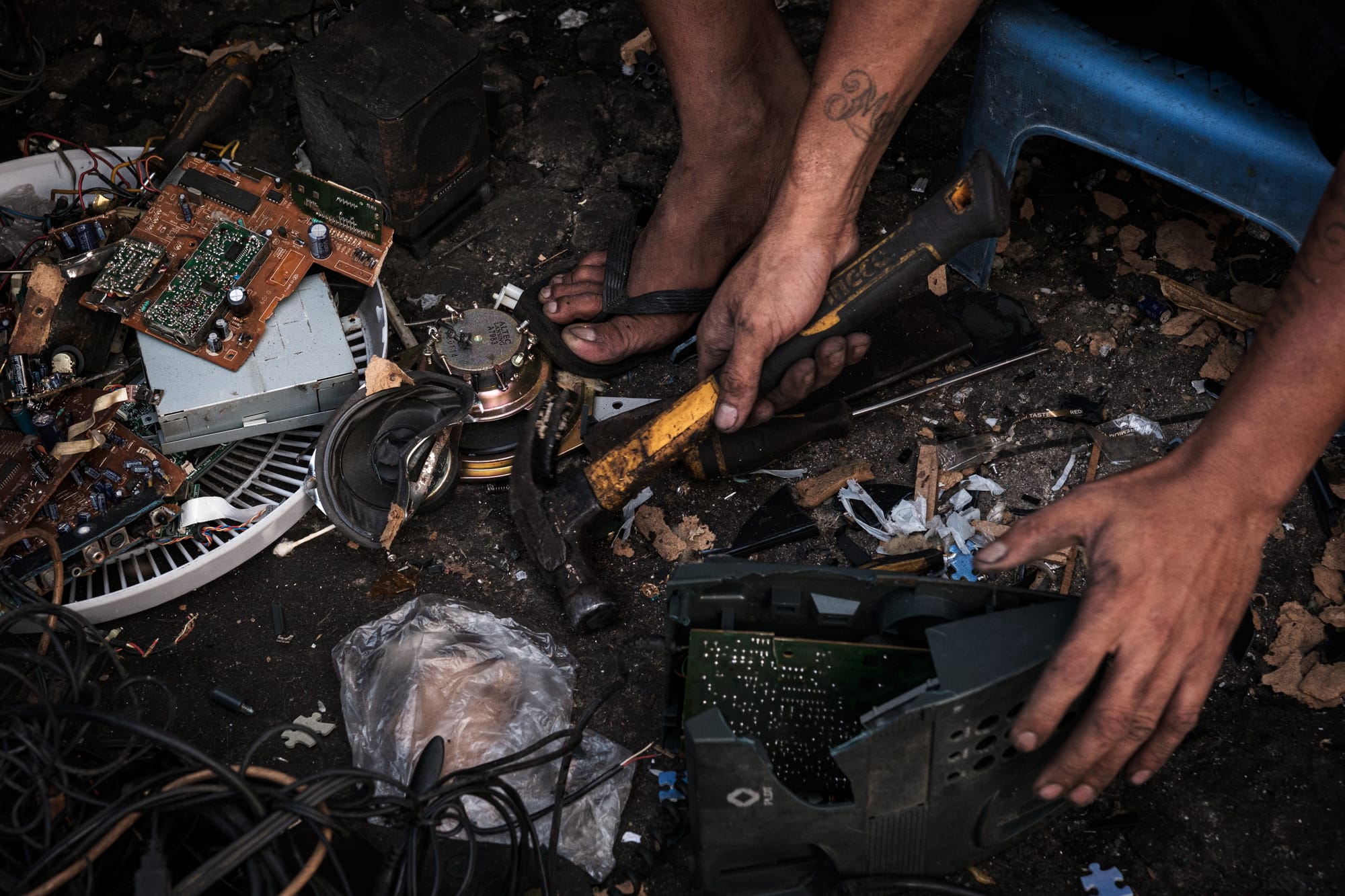 A worker holds a yellow hammer with their bare hands to smash an electronic appliance.