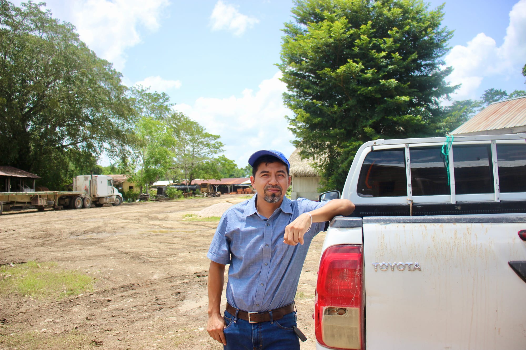Jesús stands beside a Toyota vehicle wearing a blue cap and formal clothes.
