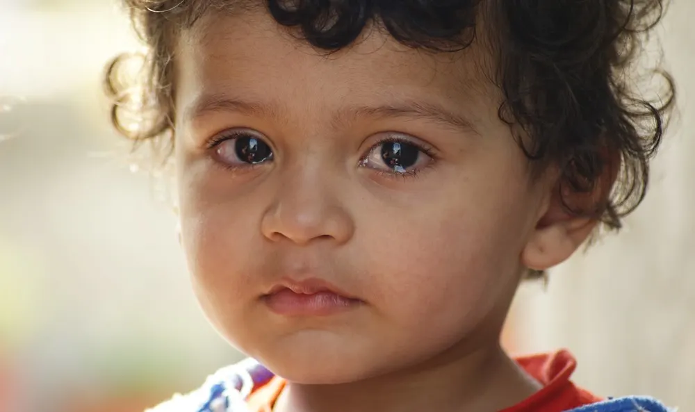 A child looks directly into the camera with tears in eyes.