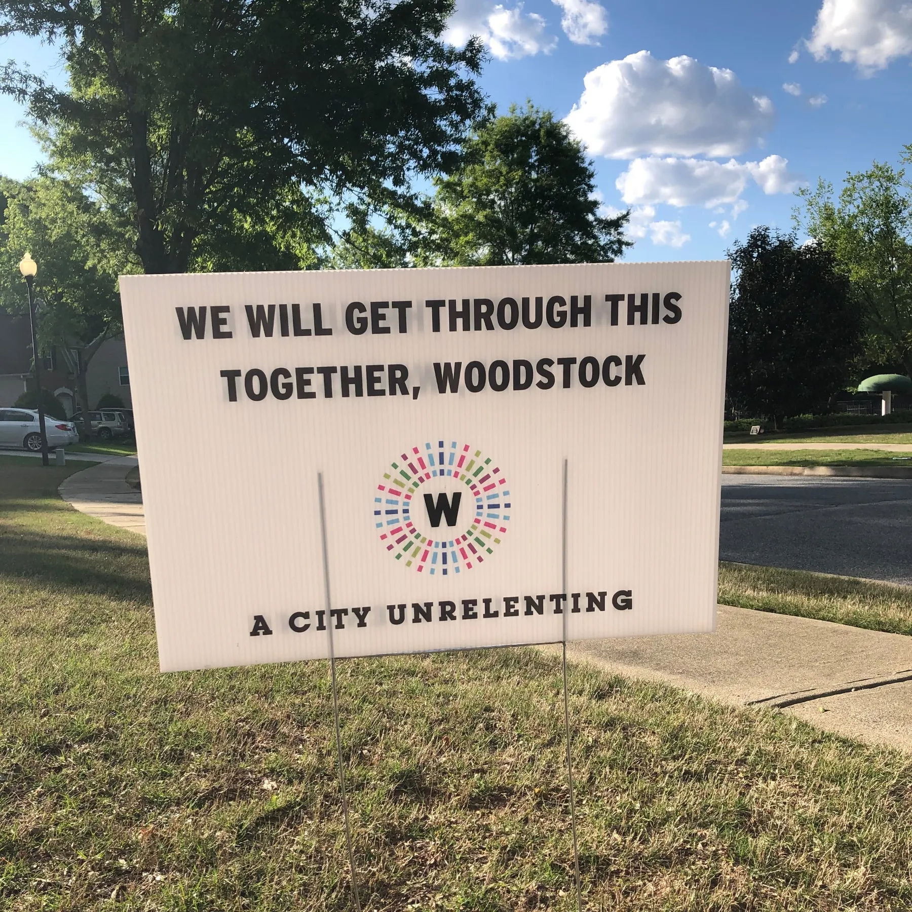 A lawn sign with the words "We will get through this together, Woodstock. A city unrelenting." 