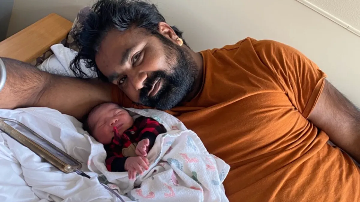 A South Asian man poses with his newborn child on a bed