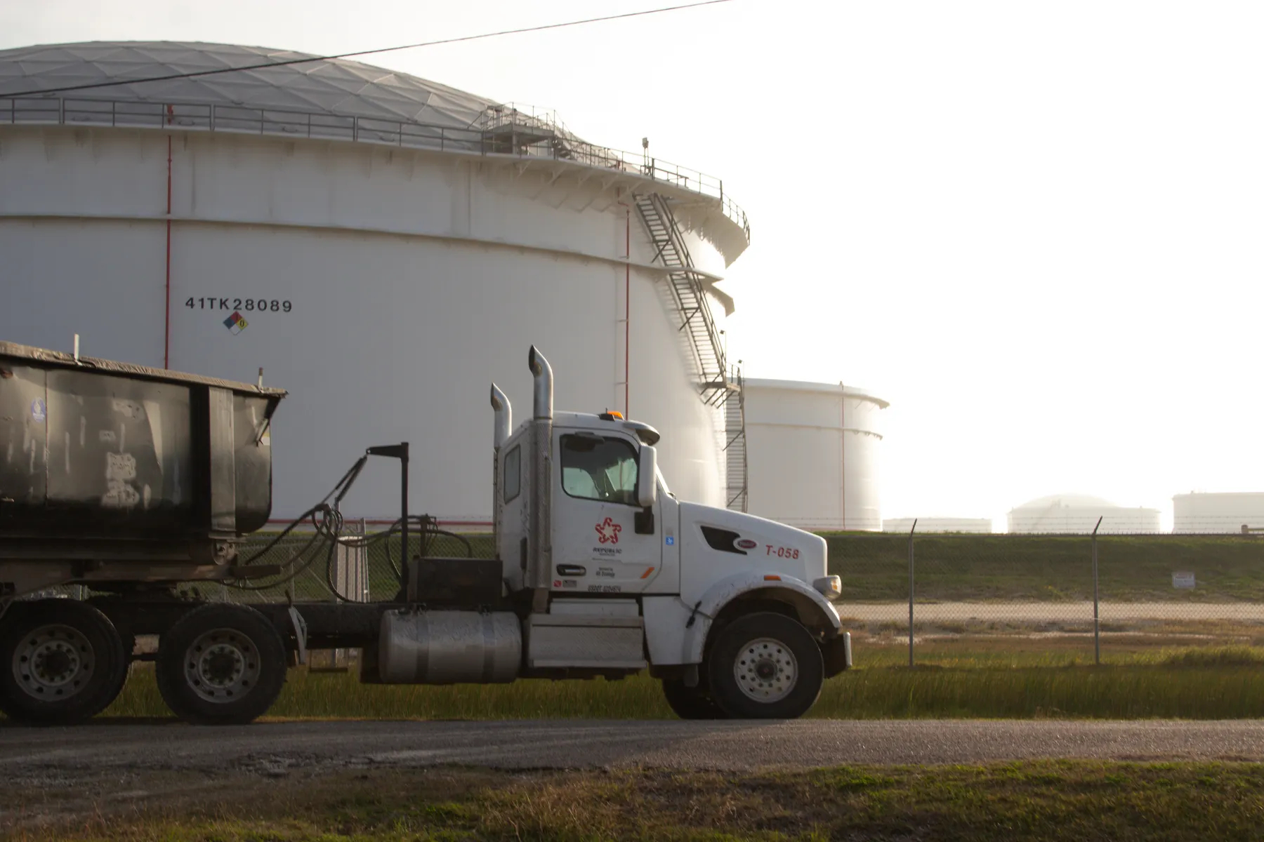 A truck passes outside oil tanks.