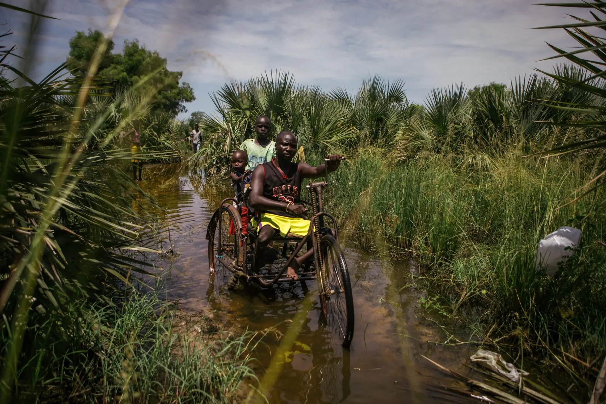 A South Sudanese family making their way through a flooded path on a tricycle